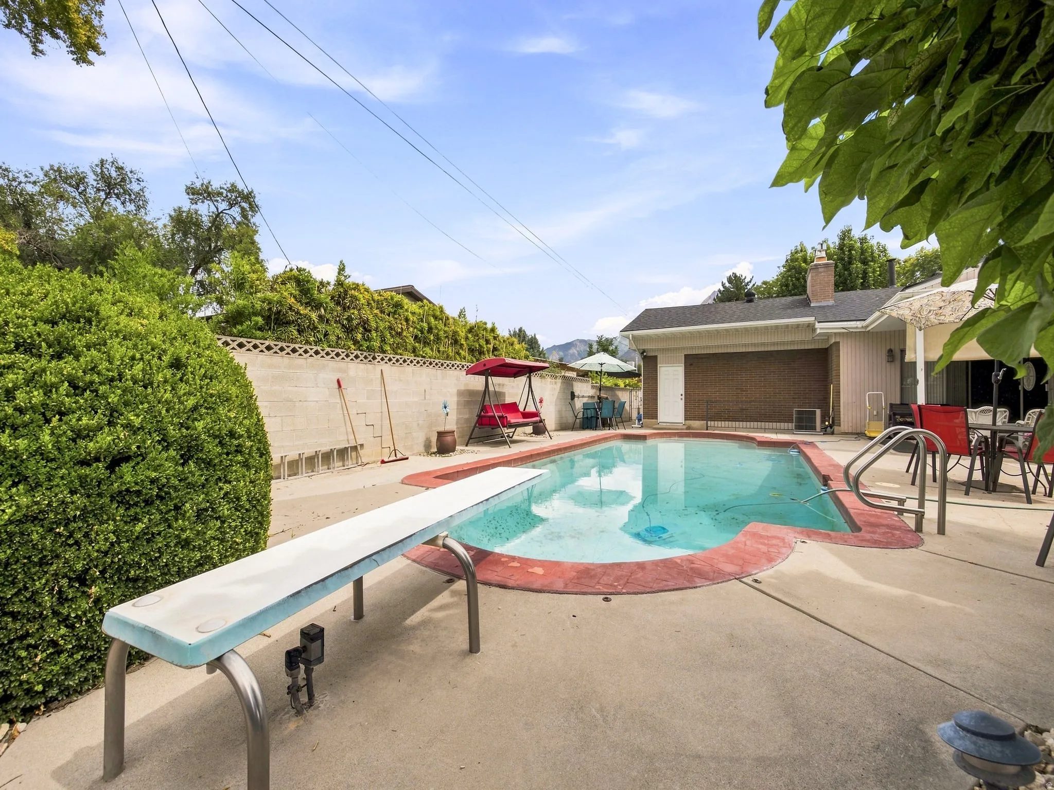 In-ground swimming pool with diving board, concrete surround, and red coping