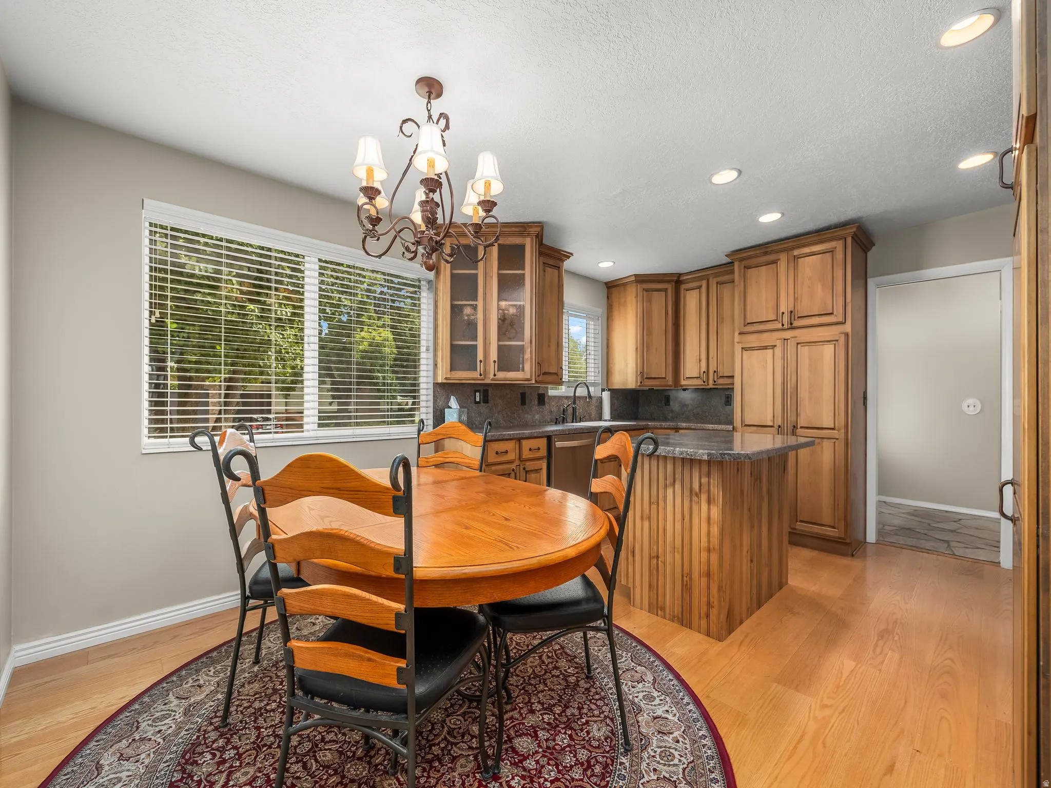 Kitchen dining area featuring a decorative chandelier, ample natural light through a large window, wood-finish cabinetry, and recessed lighting