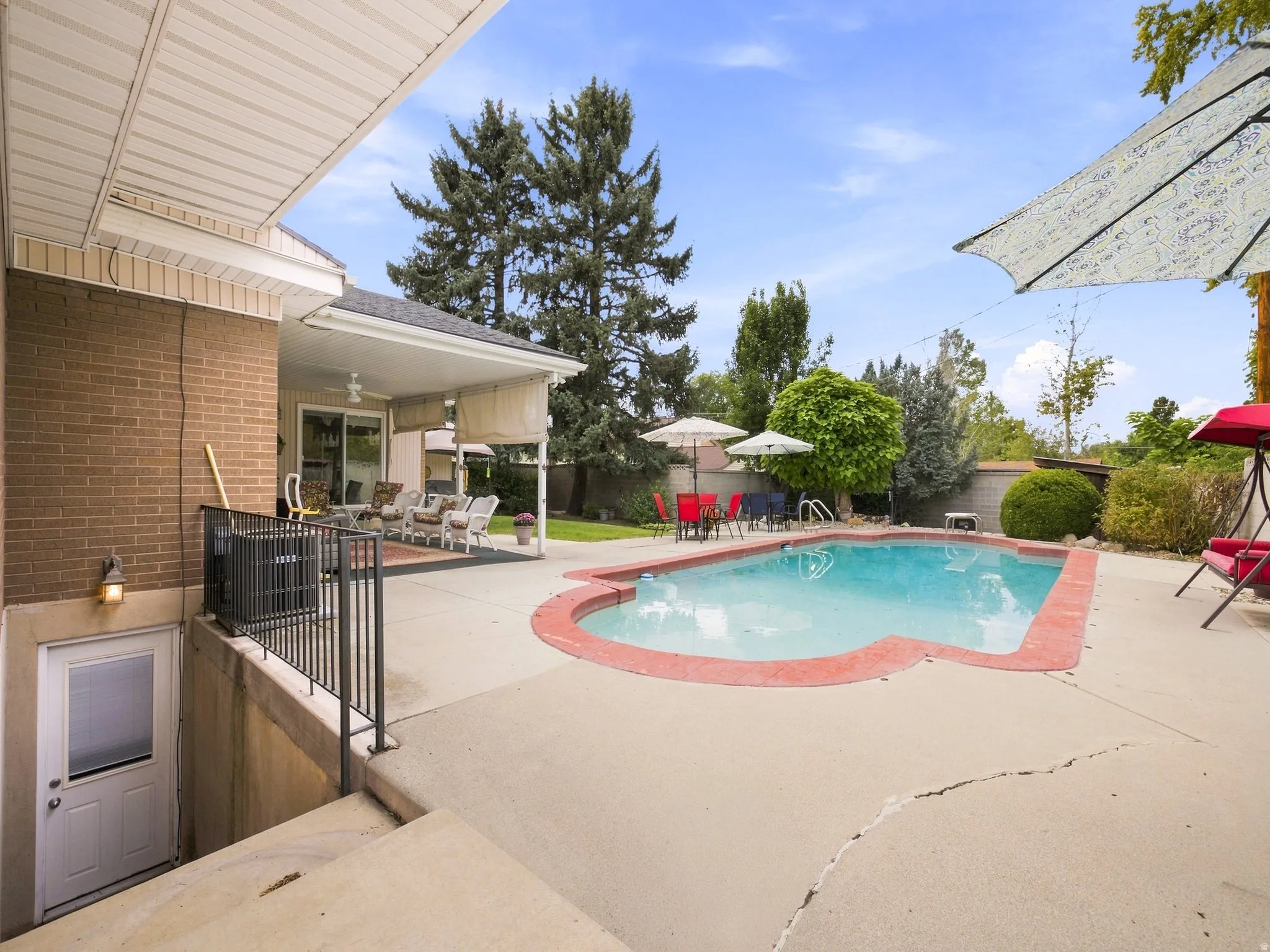 Backyard featuring a swimming pool with concrete decking, covered patio with ceiling fan, brick exterior, and mature landscaping