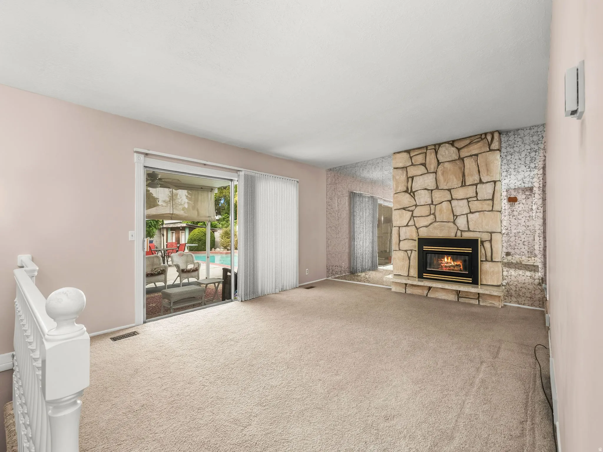 Stone-faced fireplace with hearth, mirrored wall accents, and sliding glass door to an outdoor pool area
