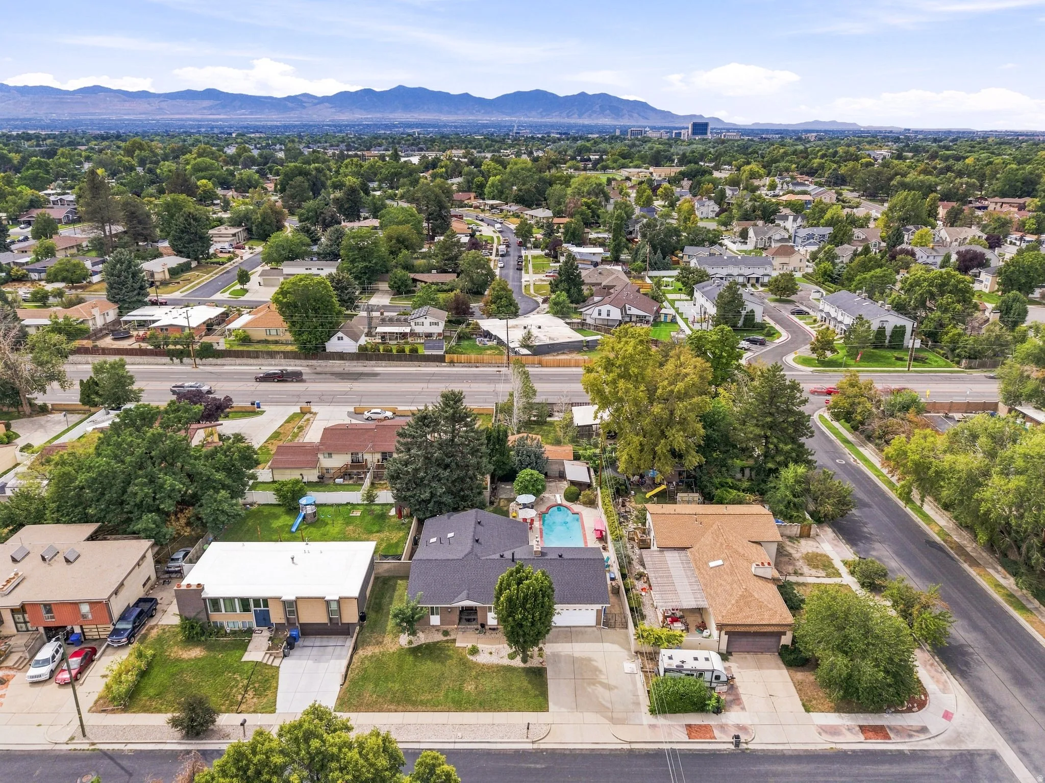 Residential neighborhood with tree-lined streets, mountain backdrop, and varying roof styles
