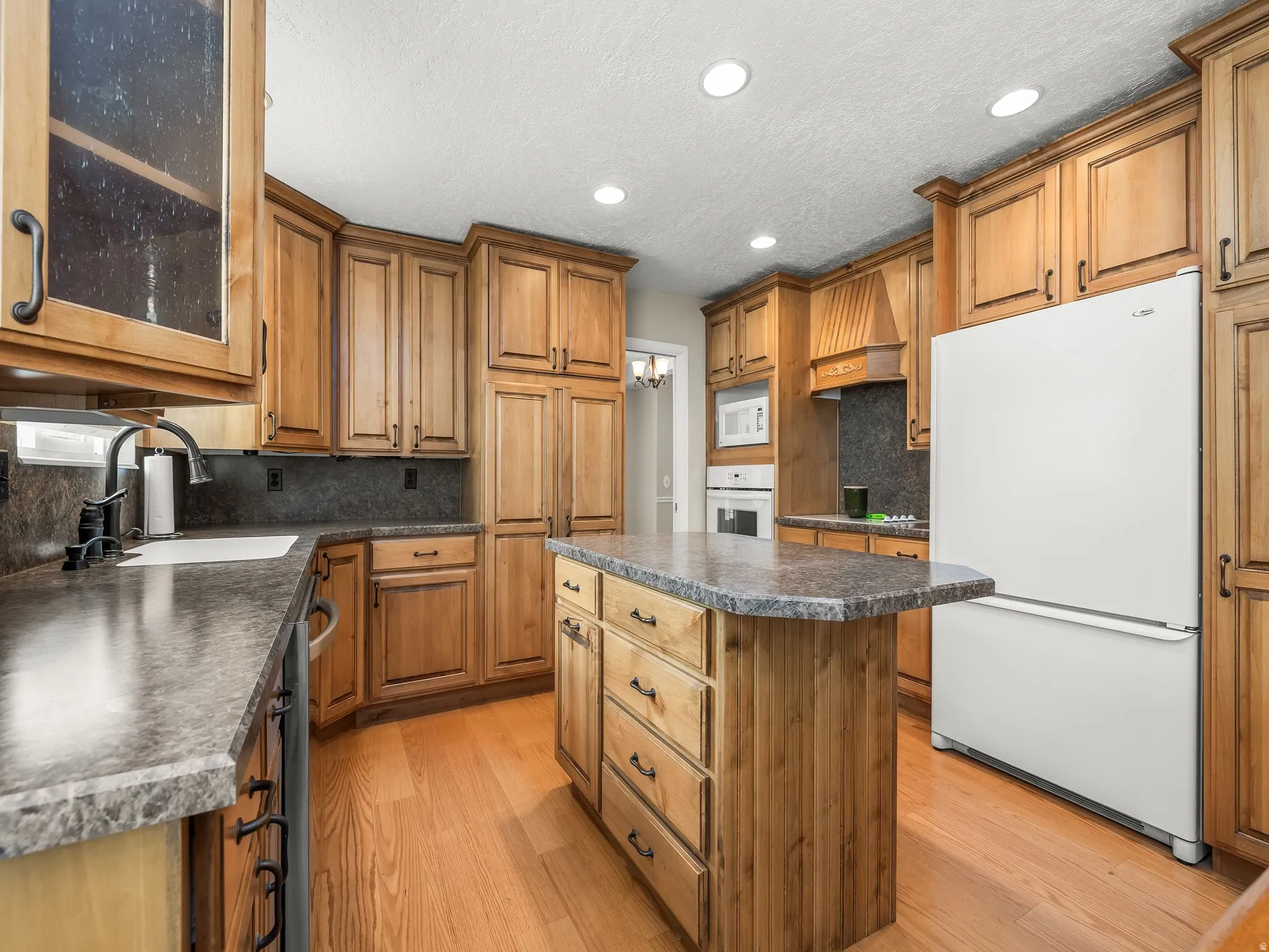 Wood-finish cabinetry, central island with storage, recessed lighting, integrated appliances, and wood-finish flooring