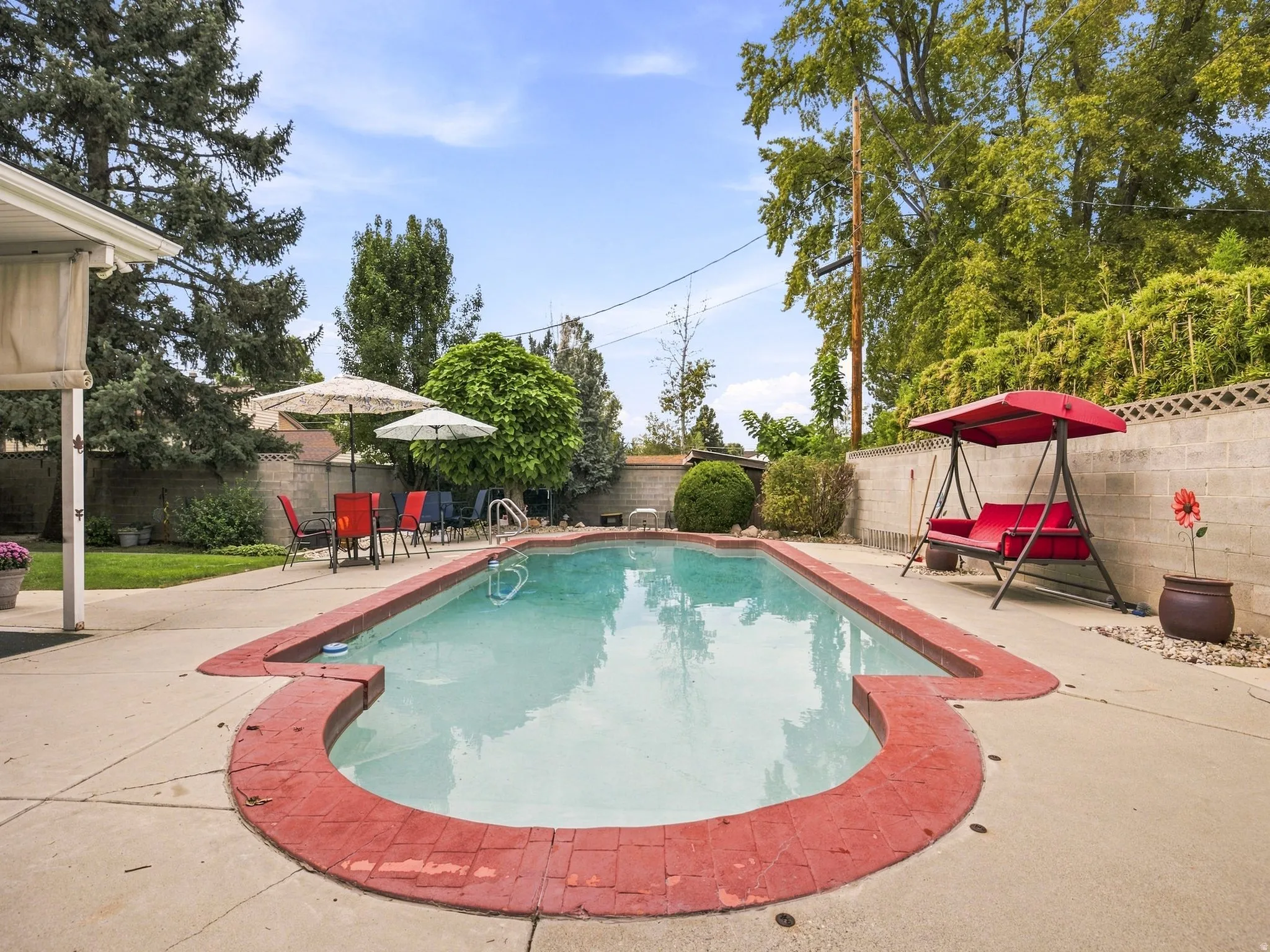 In-ground swimming pool with a red brick coping, surrounded by concrete decking and mature trees