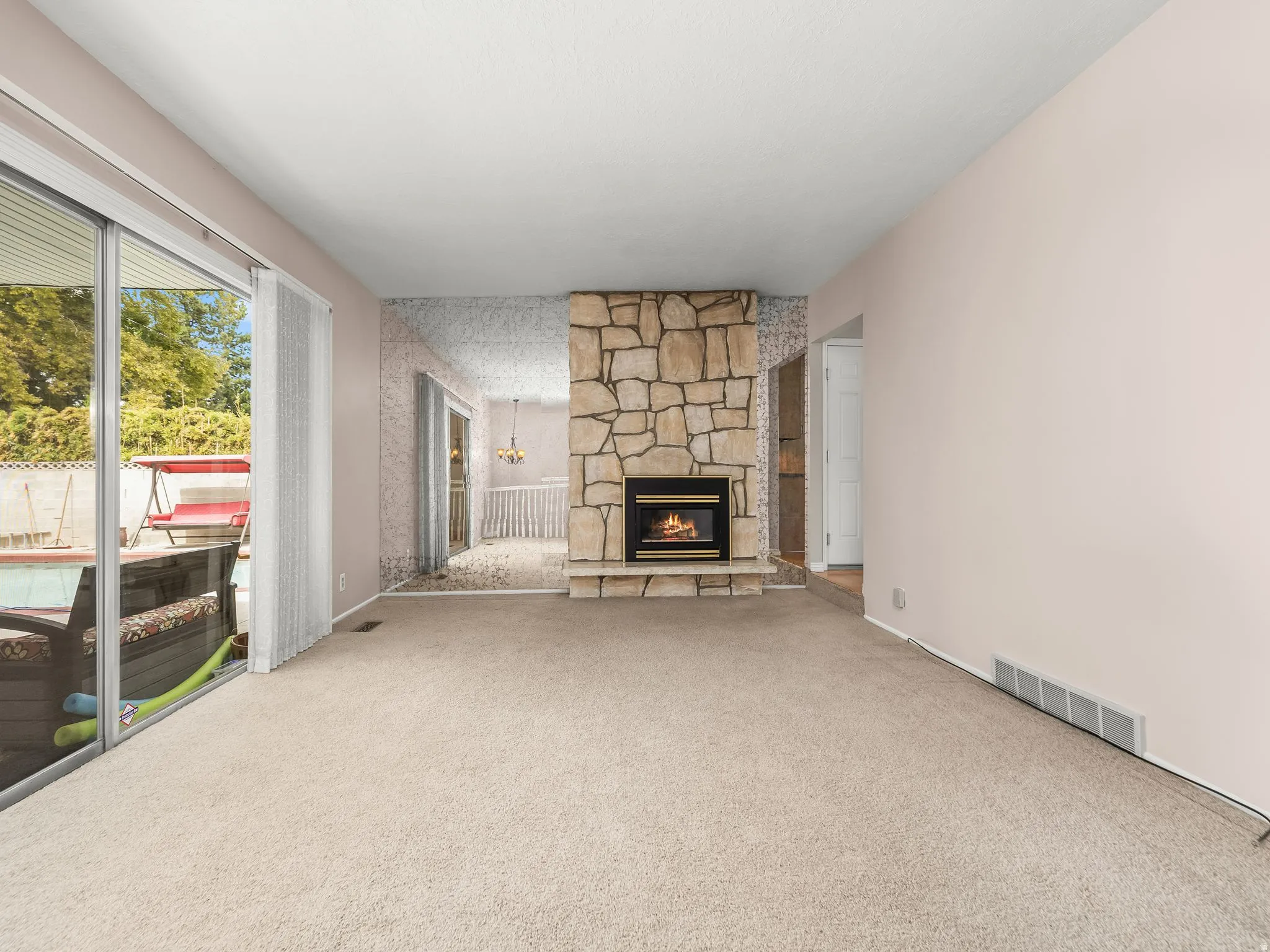 Stone-clad fireplace, large sliding glass doors, and light-toned carpeting throughout