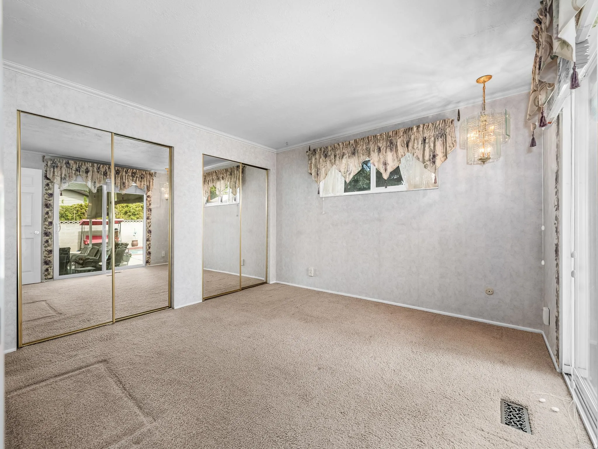 Spacious primary bedroom featuring mirrored sliding closet doors, neutral carpeting, and abundant natural light from dual windows