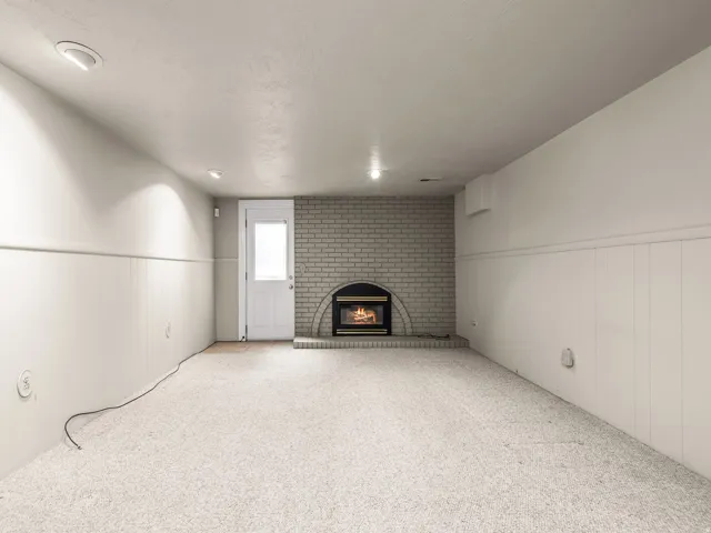 Light-colored carpeting, white wainscoting, recessed lighting, brick fireplace, and a glass-paneled door