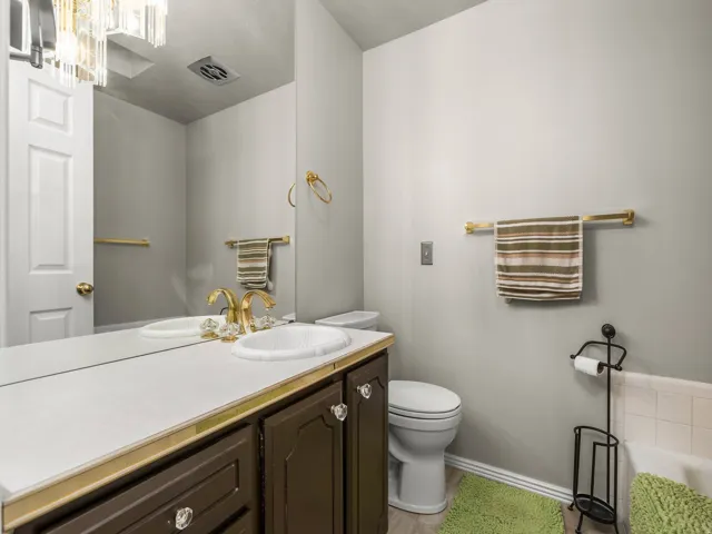 Elegant bathroom featuring a dark wood vanity with white countertop and round vessel sink, brass hardware and fixtures, large framed mirror, and tile flooring
