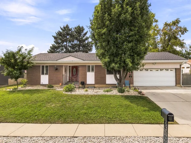 Brick exterior with white trim, an attached garage, a paved driveway, and a front lawn with mature trees and shrubbery