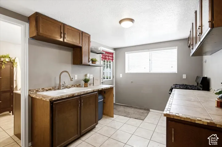 Kitchen featuring wood-finish cabinetry, tile flooring, a stainless steel faucet, and a window with blinds