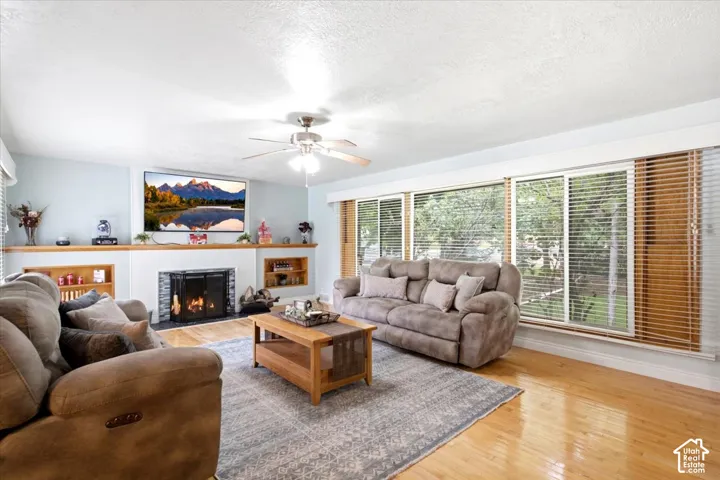 Hardwood-finish flooring, built-in fireplace with stone surround, extensive windows with blinds, ceiling fan, and built-in shelving