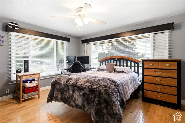 Hardwood flooring, multiple windows with blinds, ceiling fan, and painted walls