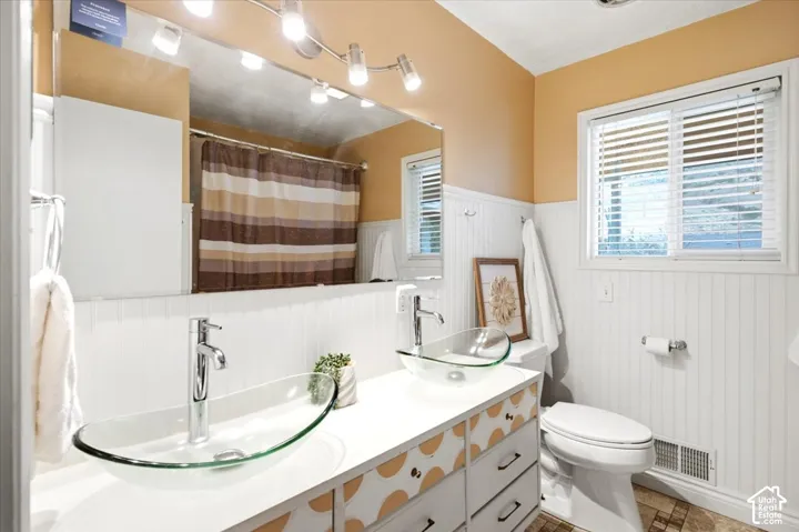 Dual vessel sinks with chrome fixtures, beadboard wainscoting, and a window with horizontal blinds