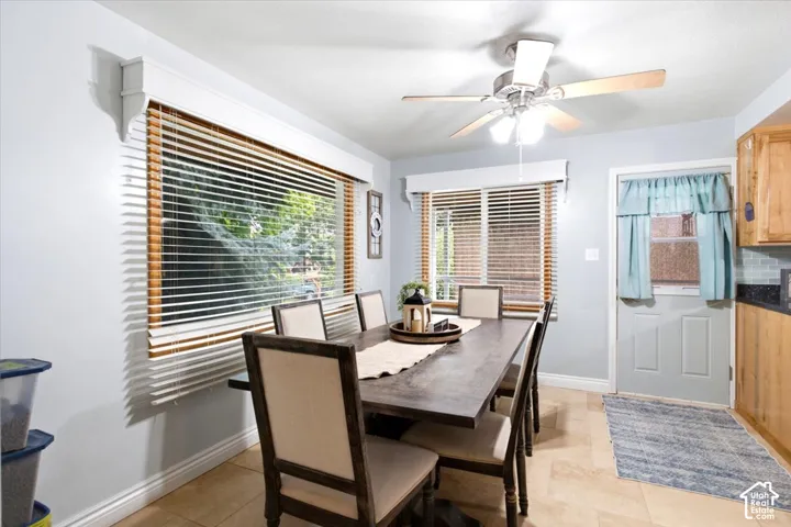 Tiled flooring, overhead ceiling fan, wooden window blinds, light wood cabinetry, and a subway tile backsplash