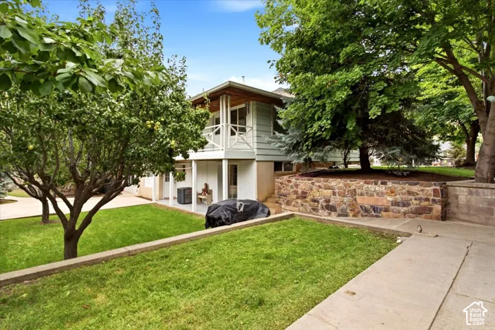 Tiered backyard with a stone retaining wall, mature trees, manicured lawn, and a concrete pathway