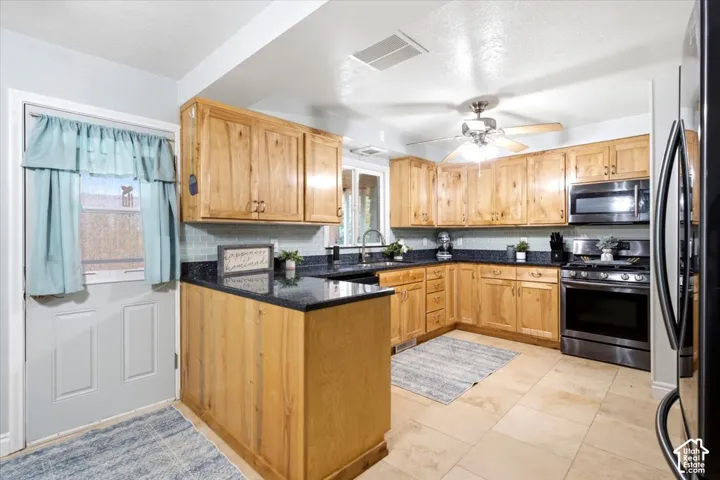 Wood-finish cabinetry complemented by dark countertops, stainless steel appliances, tile flooring, and a ceiling fan