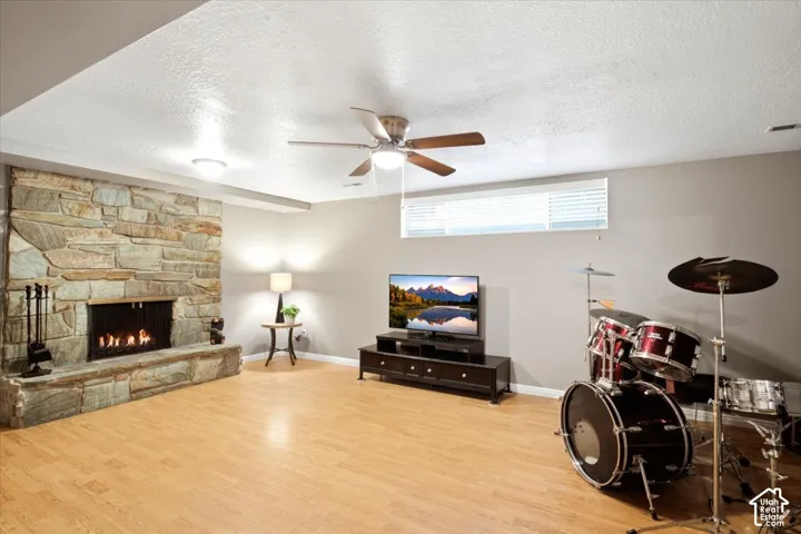 Stone-clad fireplace with hearth, wood-finish flooring, ceiling fan with integrated lighting, recessed lighting, and a horizontal window