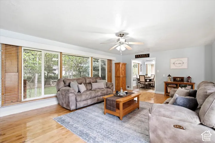 Expansive windows with wood-finish blinds, wood-finish flooring, a ceiling fan with integrated lighting, and an open doorway to a dining area
