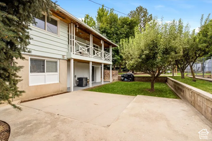 Two-story exterior with horizontal siding, an upper-level balcony featuring white cross-pattern railings, and a concrete patio