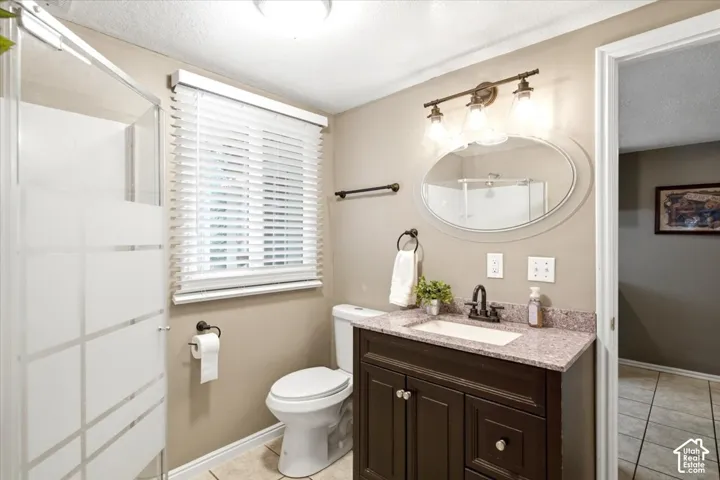 Bathroom featuring a dark wood-finish vanity with a stone countertop, an oval mirror, a three-light vanity fixture, and a glass-enclosed shower