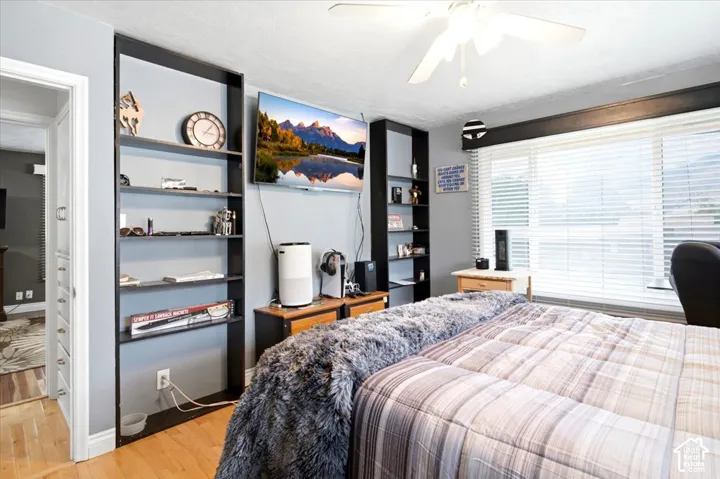 Wood-finish flooring, built-in shelving, ceiling fan, and window blinds