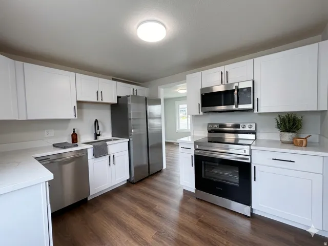 Contemporary kitchen featuring white shaker cabinetry, stainless steel appliances, wood-finish flooring, and light-toned countertops