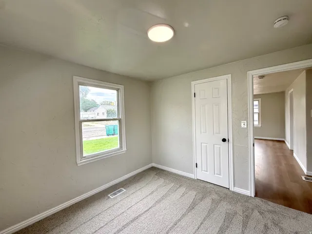 Carpeted flooring, white trim, single window, paneled door, and ceiling-mounted light fixture
