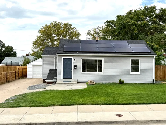 Light gray siding exterior with a dark gray front door, black roof with solar panels, and an attached garage