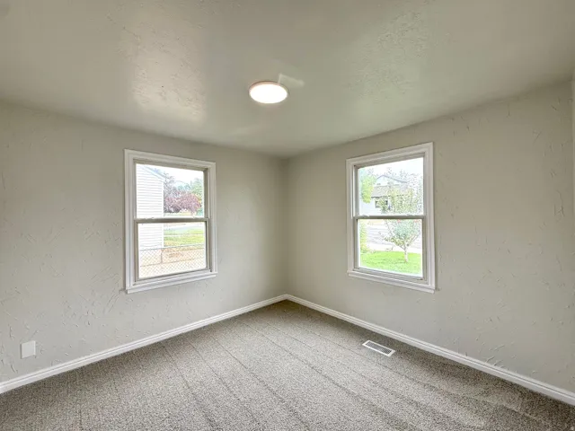 Neutral-toned walls, recessed ceiling light, dual windows with white trim, and gray patterned carpeting