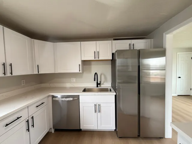White shaker cabinetry with matte black hardware, stainless steel appliances, light-toned countertops, and wood-finish flooring