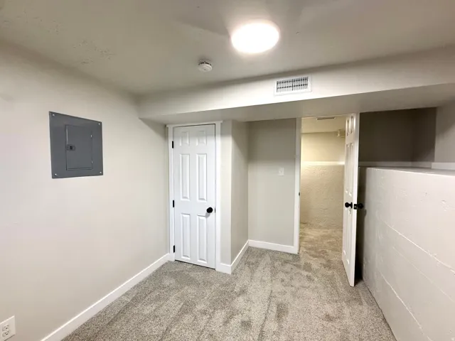 Neutral paint palette, textured carpet flooring, six-panel interior door, flush-mount ceiling light, and overhead ventilation