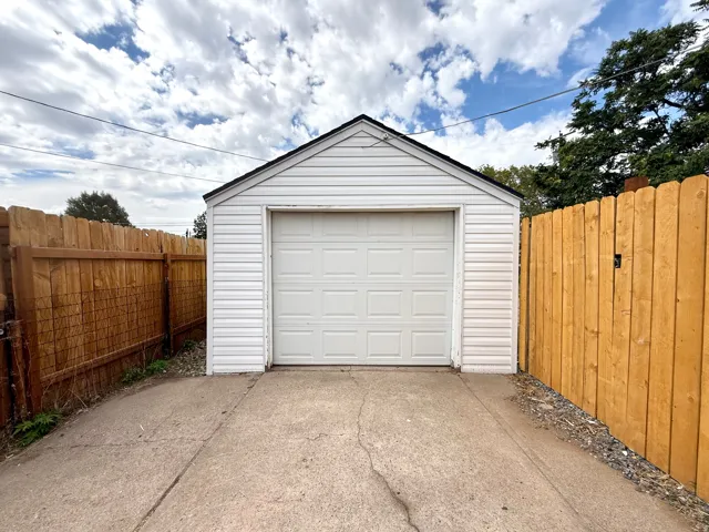 Detached garage with white siding and a panel-style garage door
