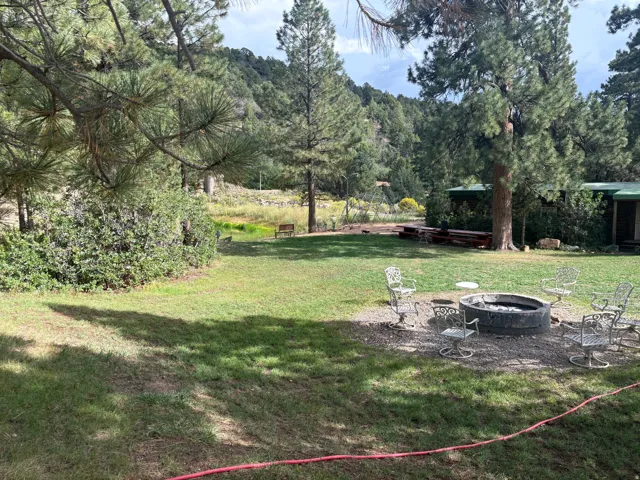 Expansive lawn area with mature trees, a built-in fire pit, and a gravel seating area