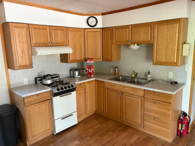 Wood-finish cabinetry, solid surface countertops, double basin stainless steel sink, and wood-finish flooring