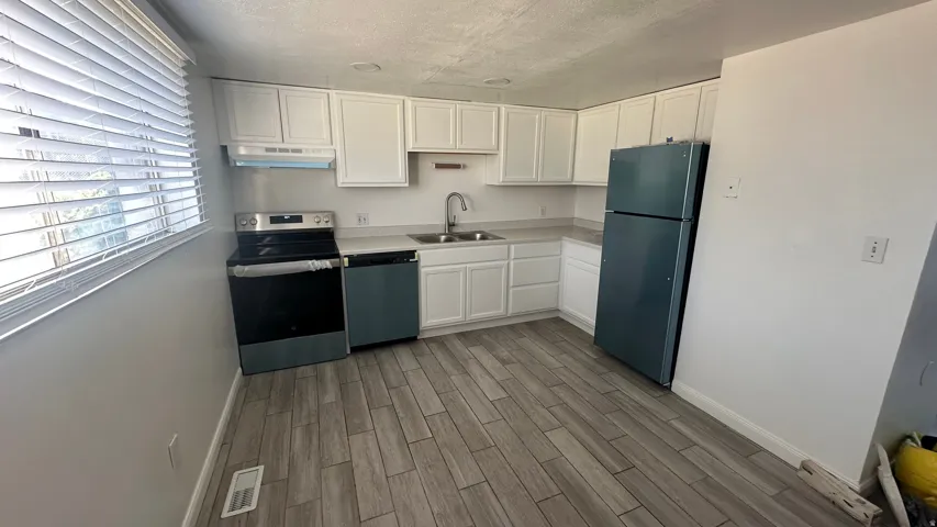 White shaker-style cabinetry, wood-finish flooring, stainless steel sink, and a built-in range with an overhead microwave