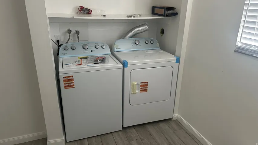 Laundry area featuring a built-in shelf, washer and dryer, and wood-finish flooring