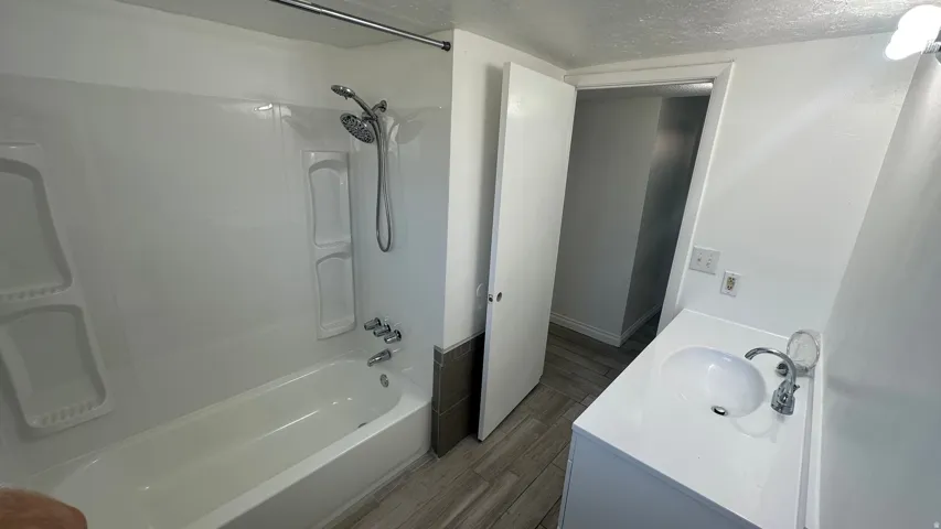 White bathtub with an integrated shower, chrome fixtures, and a vanity featuring an oval sink