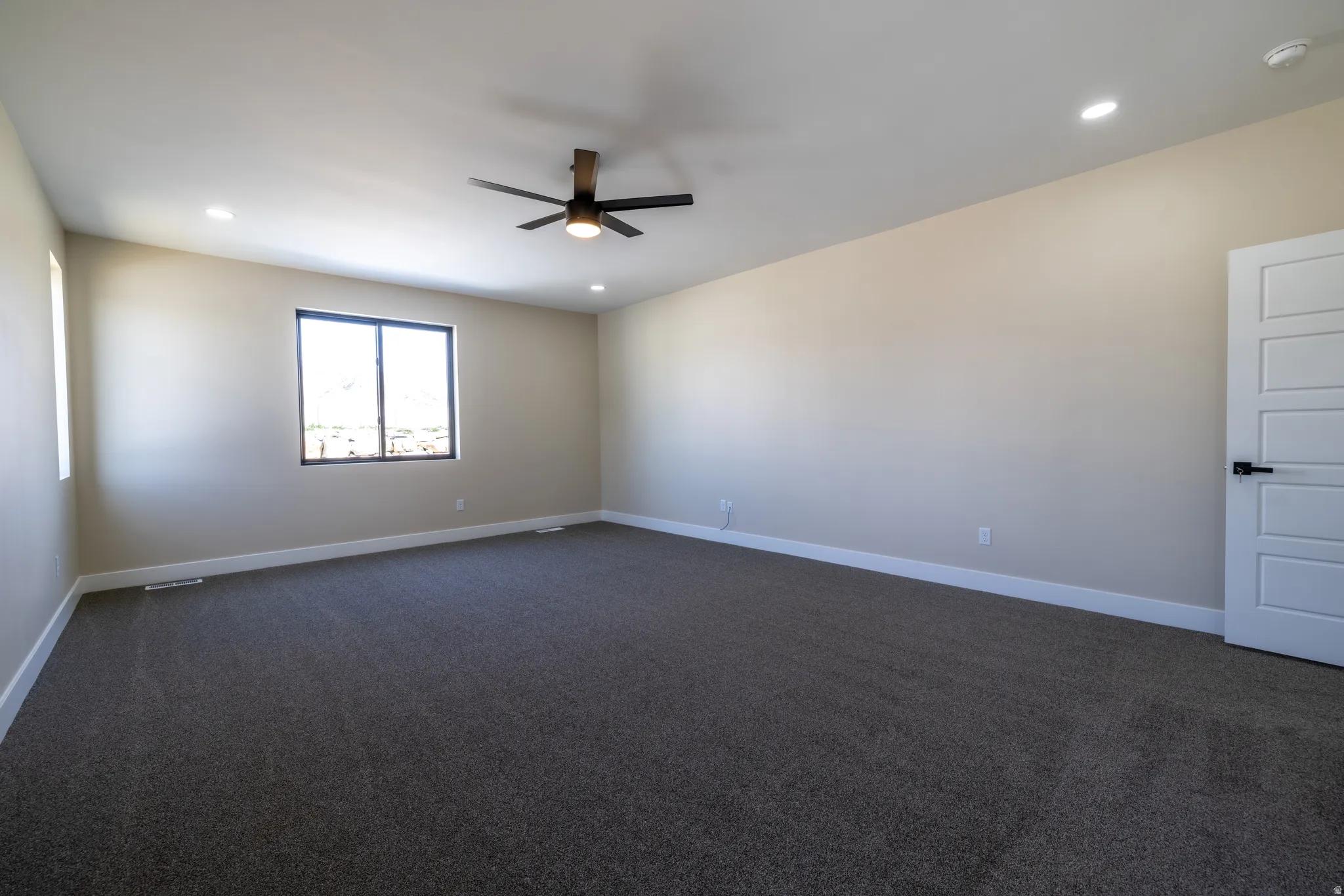 Recessed lighting, dark-finish ceiling fan, dark-frame windows, light-tone walls, and dark carpeting