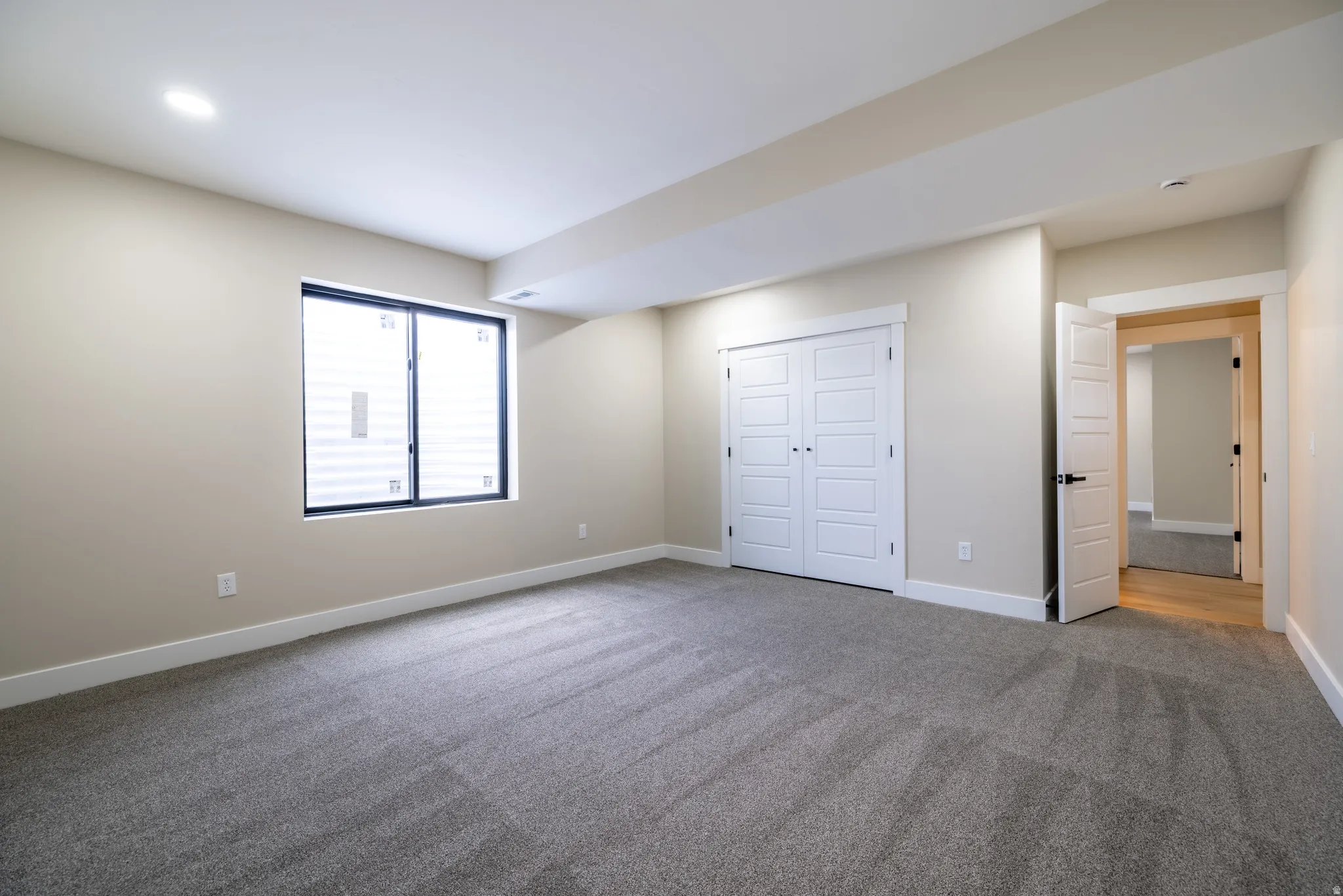 Carpeted room featuring a double-pane window, white bi-fold closet doors, recessed lighting, and neutral wall tones