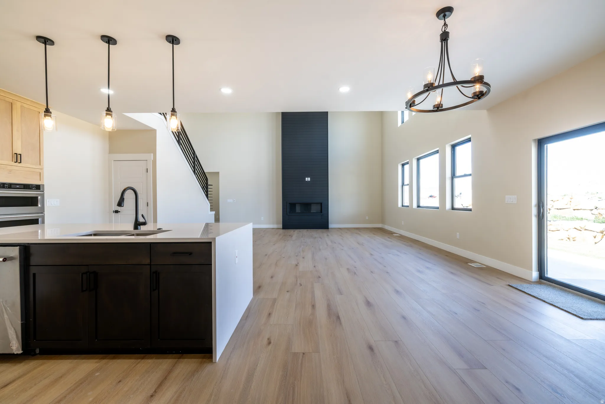 Open-concept living area featuring high ceilings, wood-finish flooring, a contemporary fireplace, and a kitchen island with a built-in sink