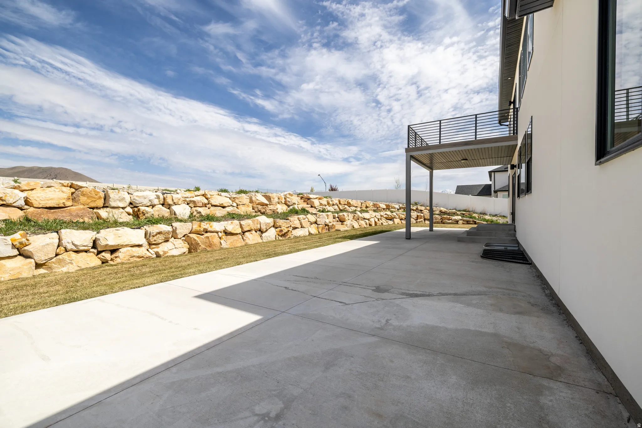 Expansive concrete patio with a retaining wall, upper-level balcony, and a covered outdoor area