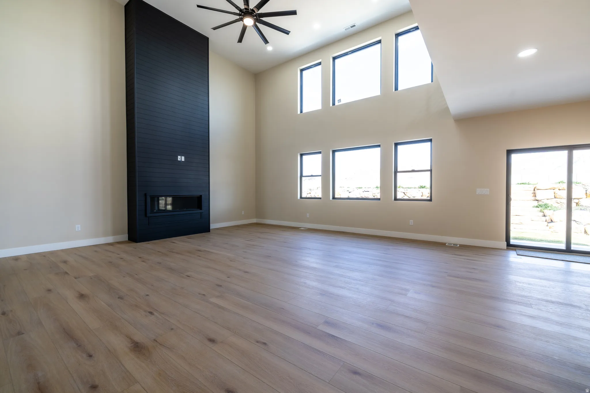 Vaulted ceilings with a ceiling fan, a tall black shiplap fireplace with an electric insert, wood-finish flooring, and multiple windows with black trim