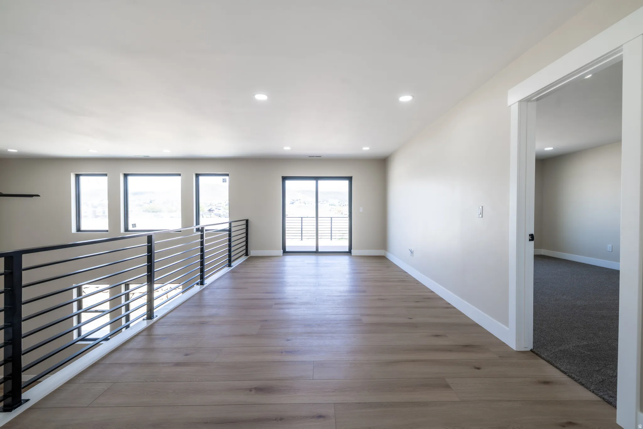 Spacious open loft area featuring wood-finish flooring, recessed lighting, and a modern horizontal metal railing