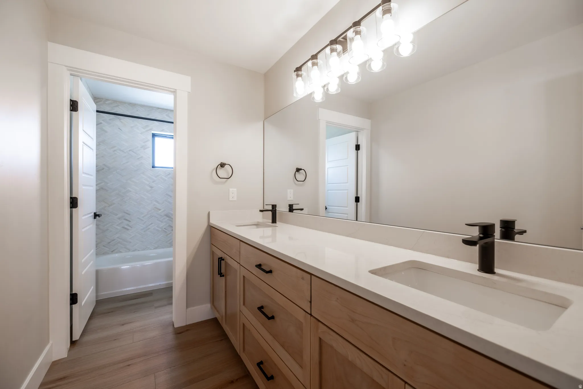 Dual vanity with integrated sinks, light wood-finish cabinetry, and matte black fixtures