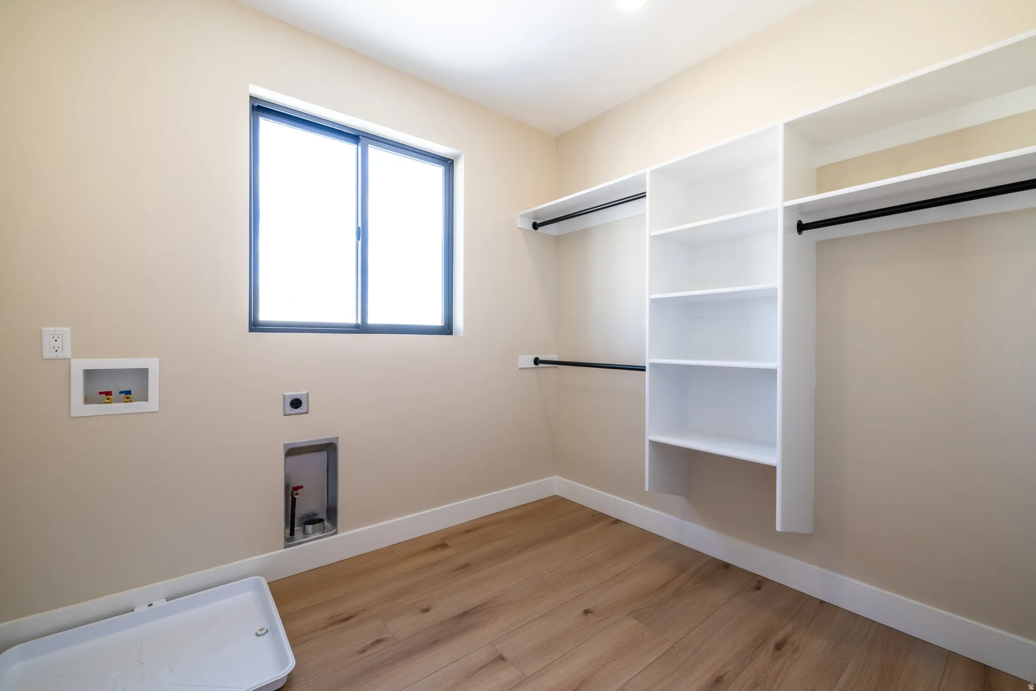 Laundry area with wood-finish flooring, a sliding window, and built-in white shelving