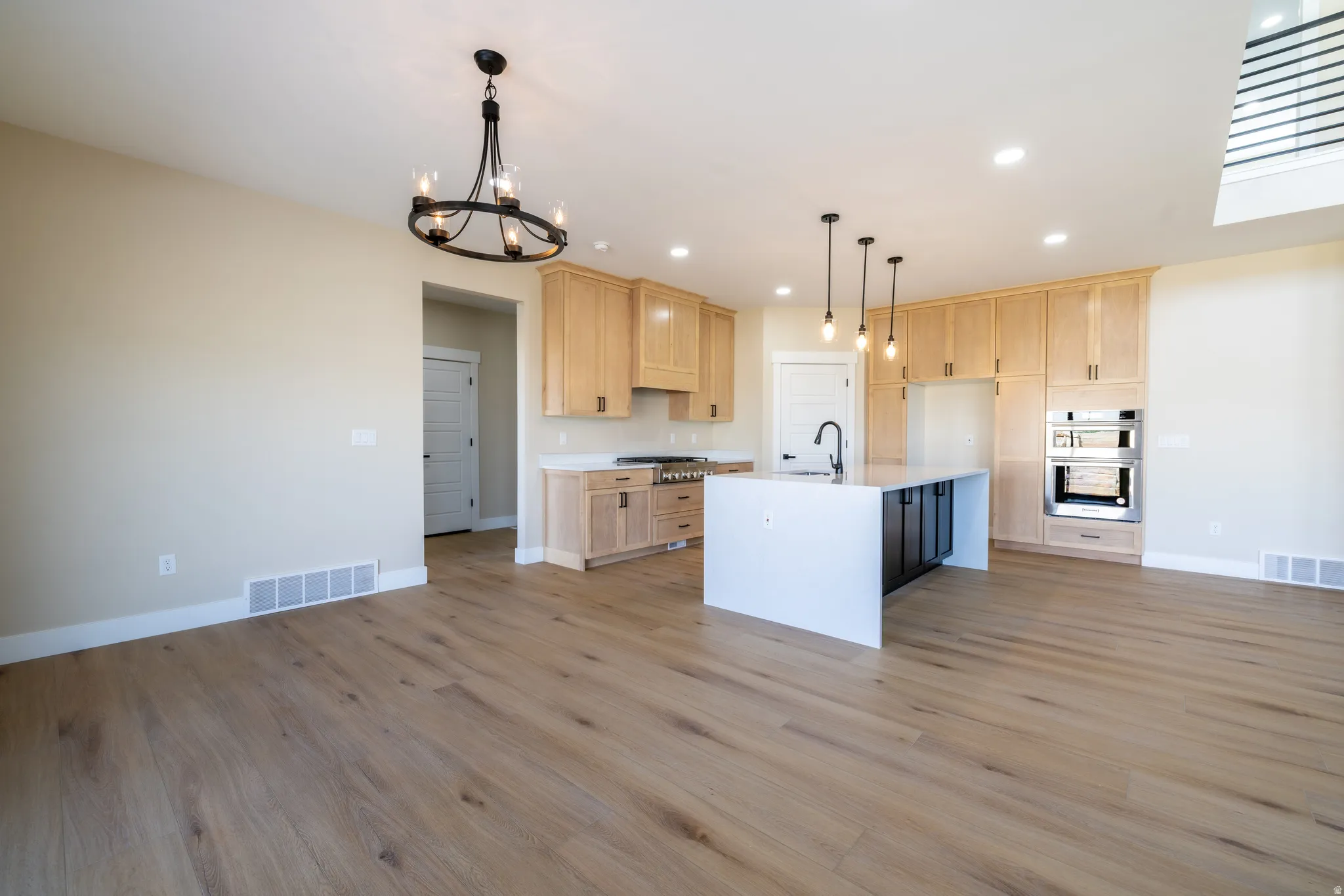 Open-concept kitchen with wood-finish flooring, light-toned cabinetry, a central island with a white countertop and dark base, stainless steel built-in appliances, and recessed lighting