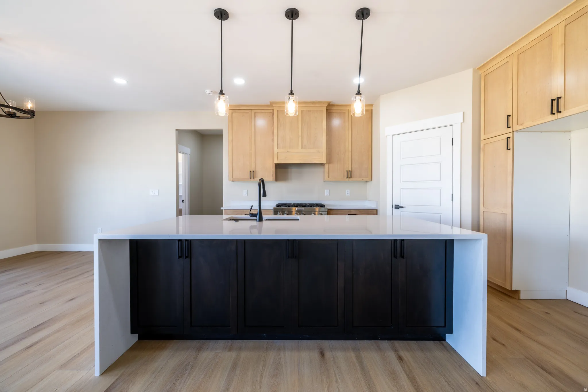 Kitchen featuring an expansive island with a light-toned countertop, wood-finish flooring, light-toned cabinetry, and matte black hardware