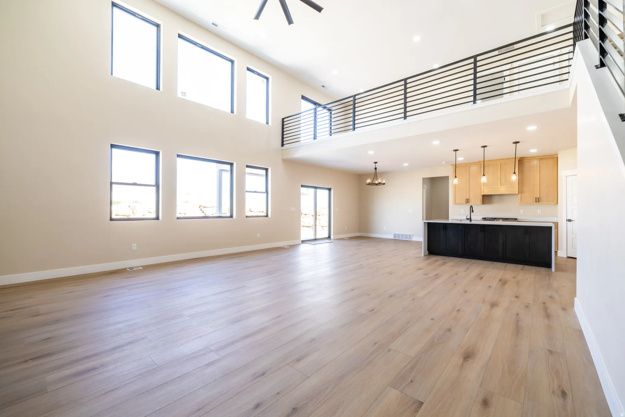 Vaulted ceilings with abundant natural light, wood-finish flooring, a kitchen island with stone countertops, and a modern horizontal railing system