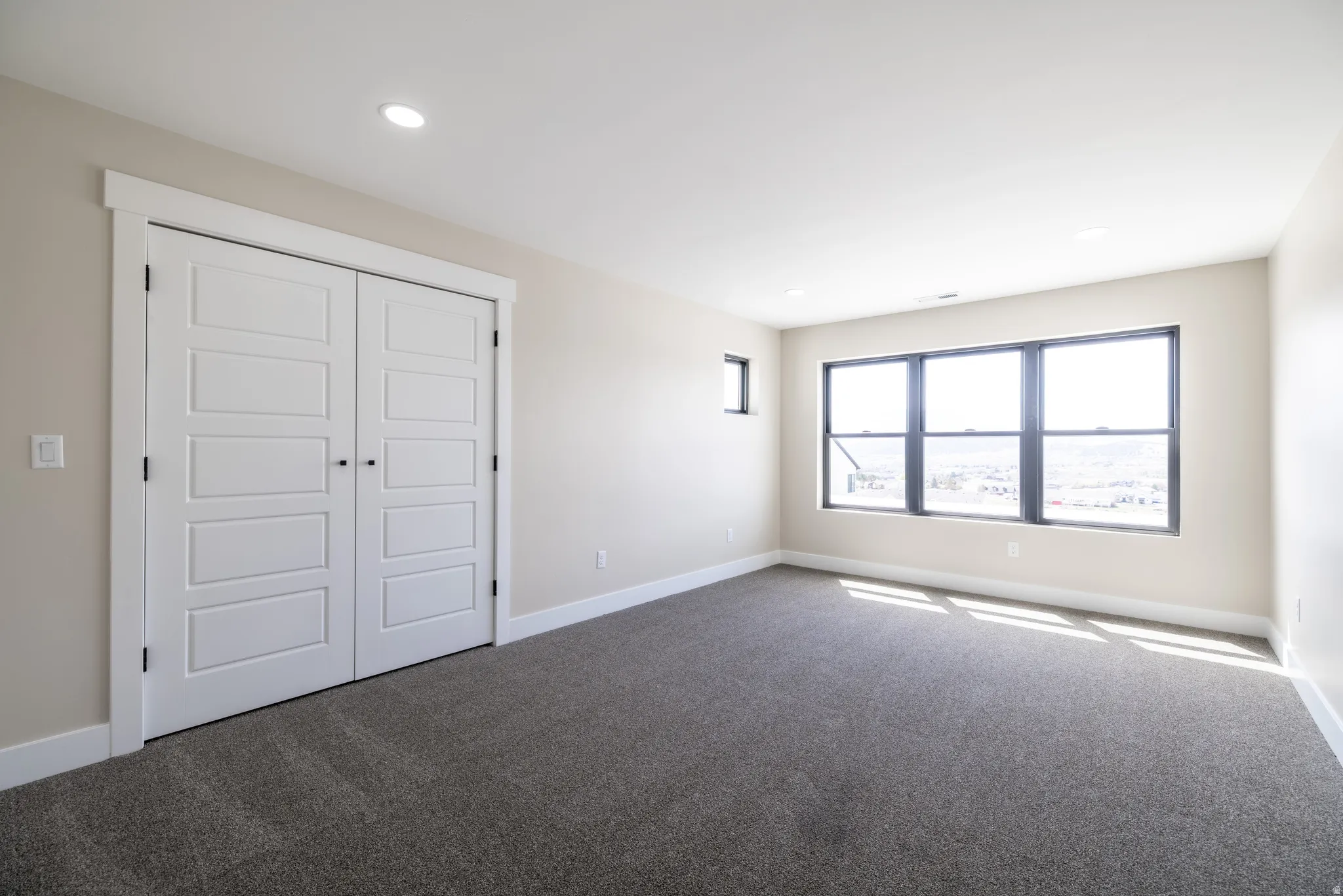 Spacious room with gray carpeting, white walls, recessed ceiling lighting, and a large multi-pane window