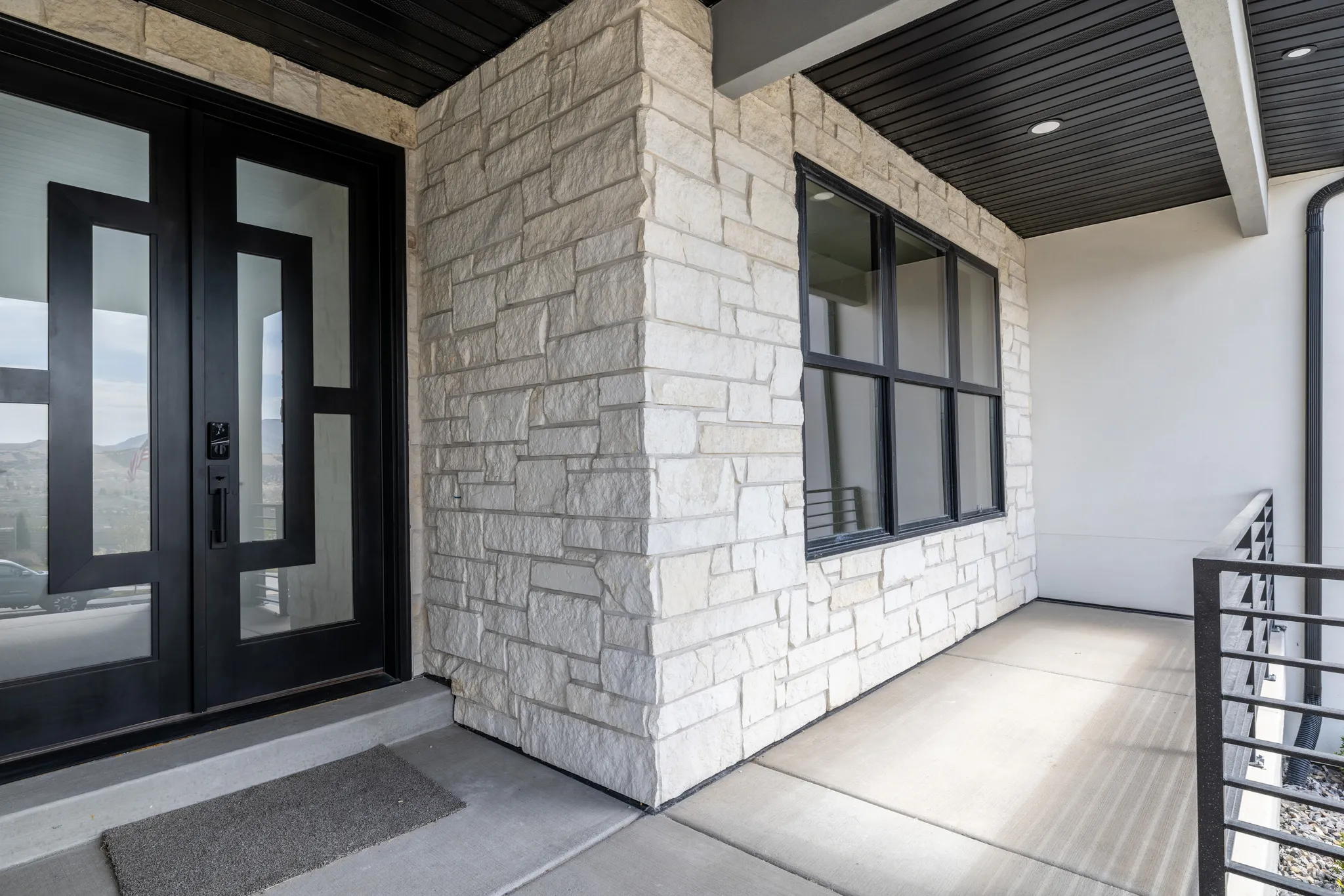 Stone veneer exterior with a concrete porch, featuring a double entry door with geometric glass panels and black-framed windows