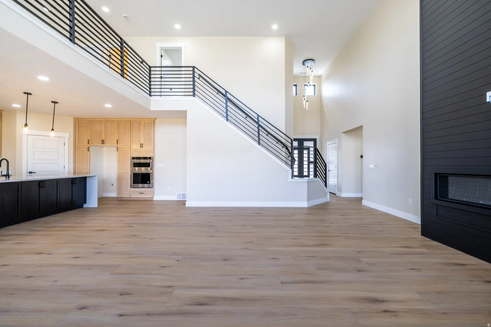 Open-concept living space featuring wood-finish flooring, a two-story ceiling, and a contemporary fireplace with a black shiplap surround